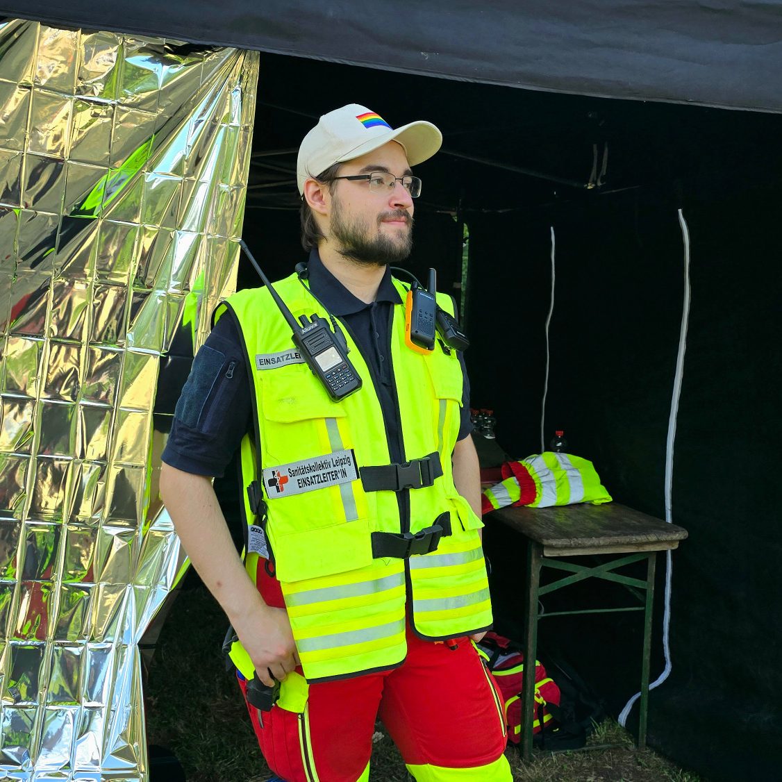 Ein Sanitäter in Einsatzkleidung steht am Eingang eines Zeltes das als Unfallhilfsstelle dient. Er hat 2 Funkgeräte dabei.