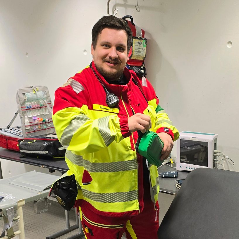 Ein Sanitäter in rot-gelber Einsatzkleidung richtet eine Unfallhilfsstelle mir Notfallrucksack, EKG, Tragen und anderem Einsatzmaterial ein.