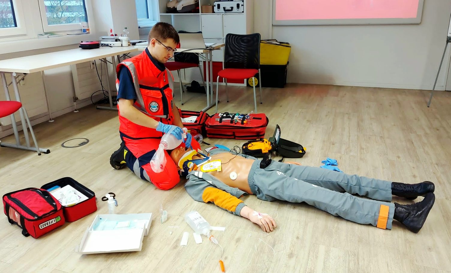 Ein Sanitäter leistet Erste Hilfe an einer simulierten Person in einem Schulungsraum.