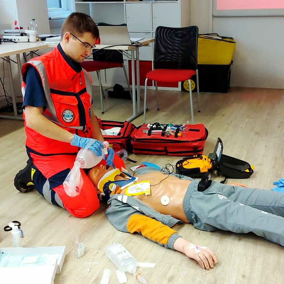 Eine Sanitätsausbildung, in der ein Ausbilder einen Dummy mit medizinisch behandelt und Teilnehmer*innen erklärt was er tut.