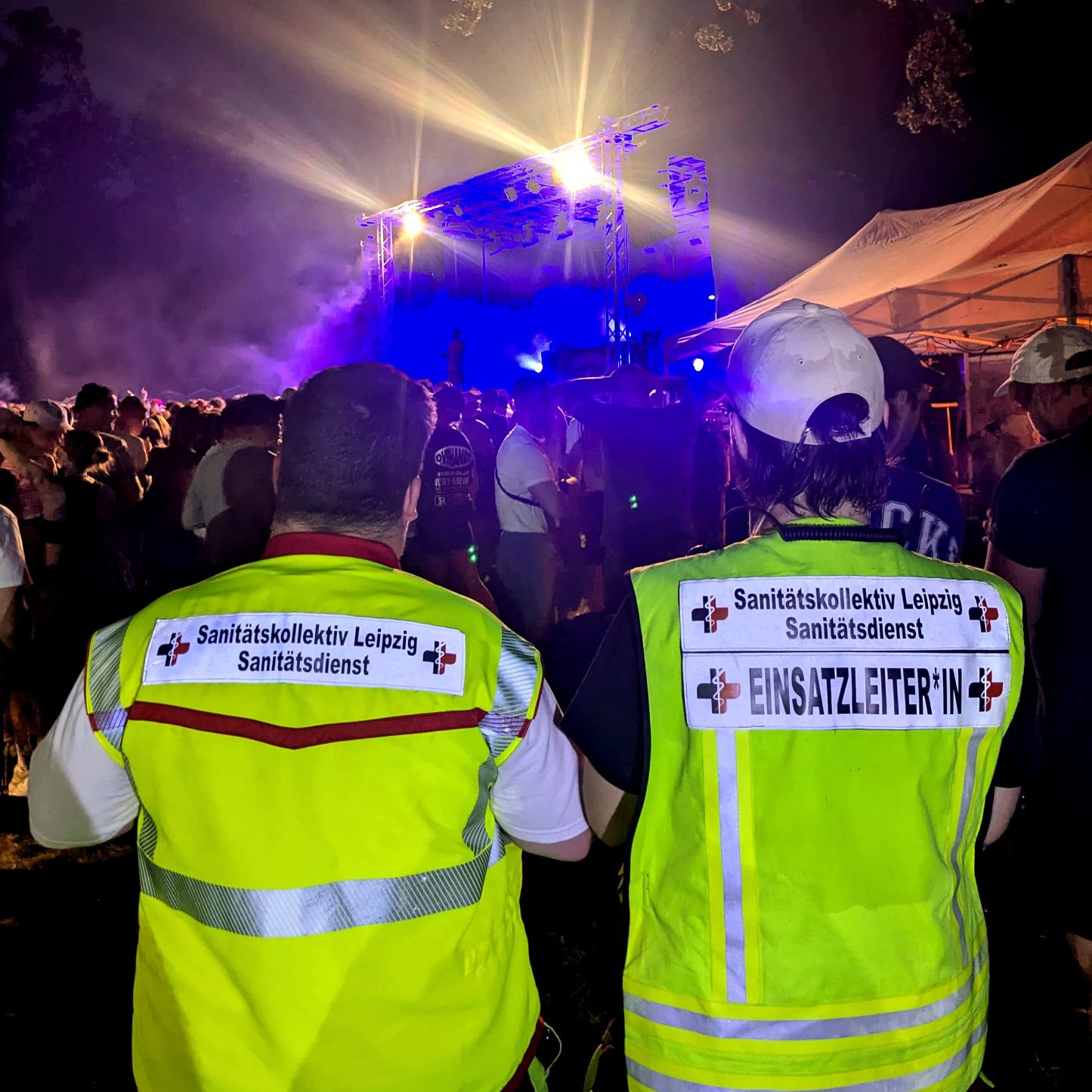 Eine Einsatzkraft und die Einsatzleitung stehen vor einer feiernden Menge, welche einem Konzert beiwohnt.