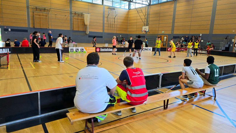 Zwei Helfer*innen des SKL sitzen auf einer Bank und beobachten das Turnier der Schüler*innen in Floorball und Basketball.