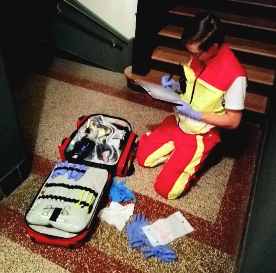 Ein Sanitäter kniet neben einem offenen Notfallkoffer und notiert Informationen.