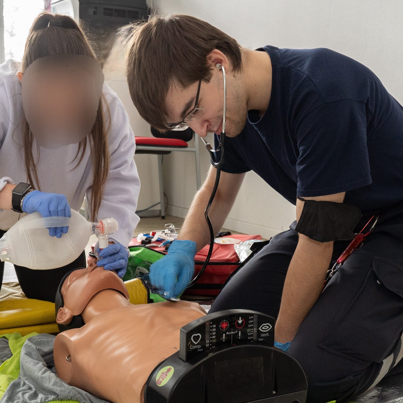 In einer Sanitätsausbildung intubiert eine junge Person an einer Puppe und ein Ausbilder prüft, ob die Maßnahme korrekt durchgeführt wurde.