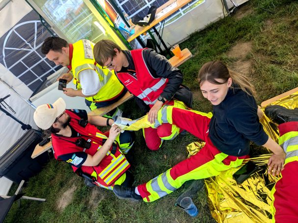 Eine Gruppe aus Sanitäter*innen sitzt in der Unfallhilfsstelle. Sie üben gegenseitig das Anlegen von SamSplint-Schienen für Knochenbrüche.