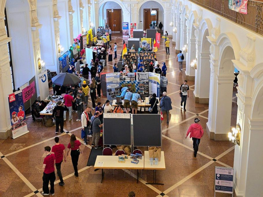Eine Übersicht der Teamstände im 2. OG. Viele Teams bauen an ihren Ständen an kleinen Robotern und reden miteinander.