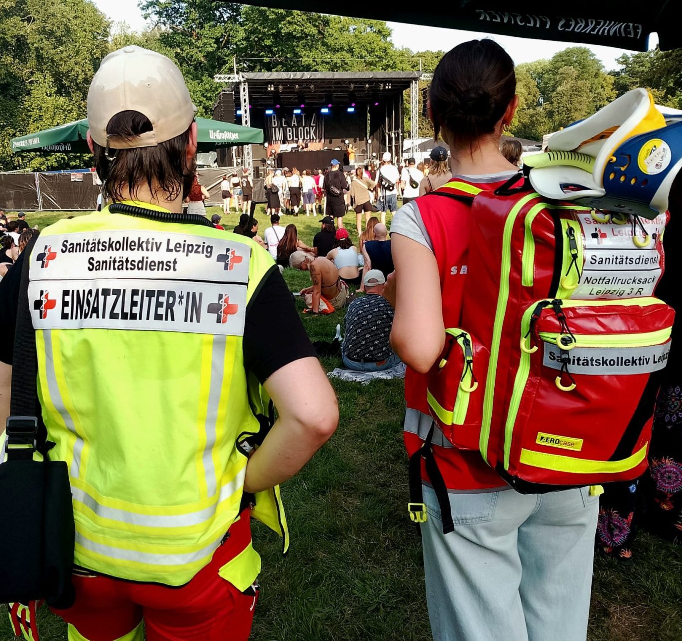 Gruppe von Sanitäter*innen steht in Einsatzkleidung am Rand eines Open-Air-Konzerts und beobachtet die Menschen.
