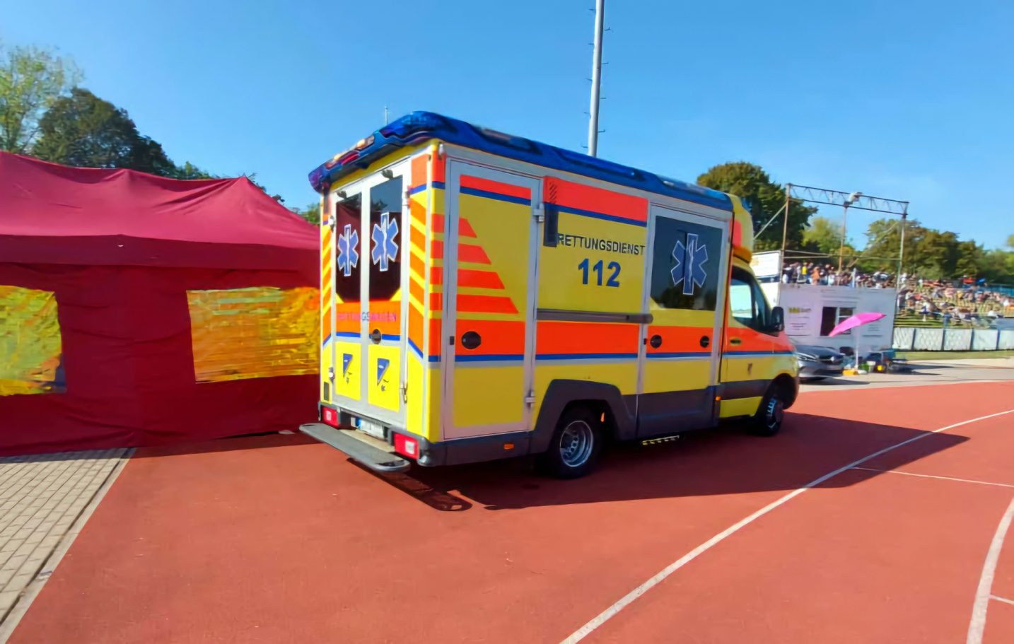 Ein Rettungswagen (RTW) steht auf einem Sportplatz neben der Unfallhilfsstelle des SKL um eine*n Patient*in zu versorgen.
