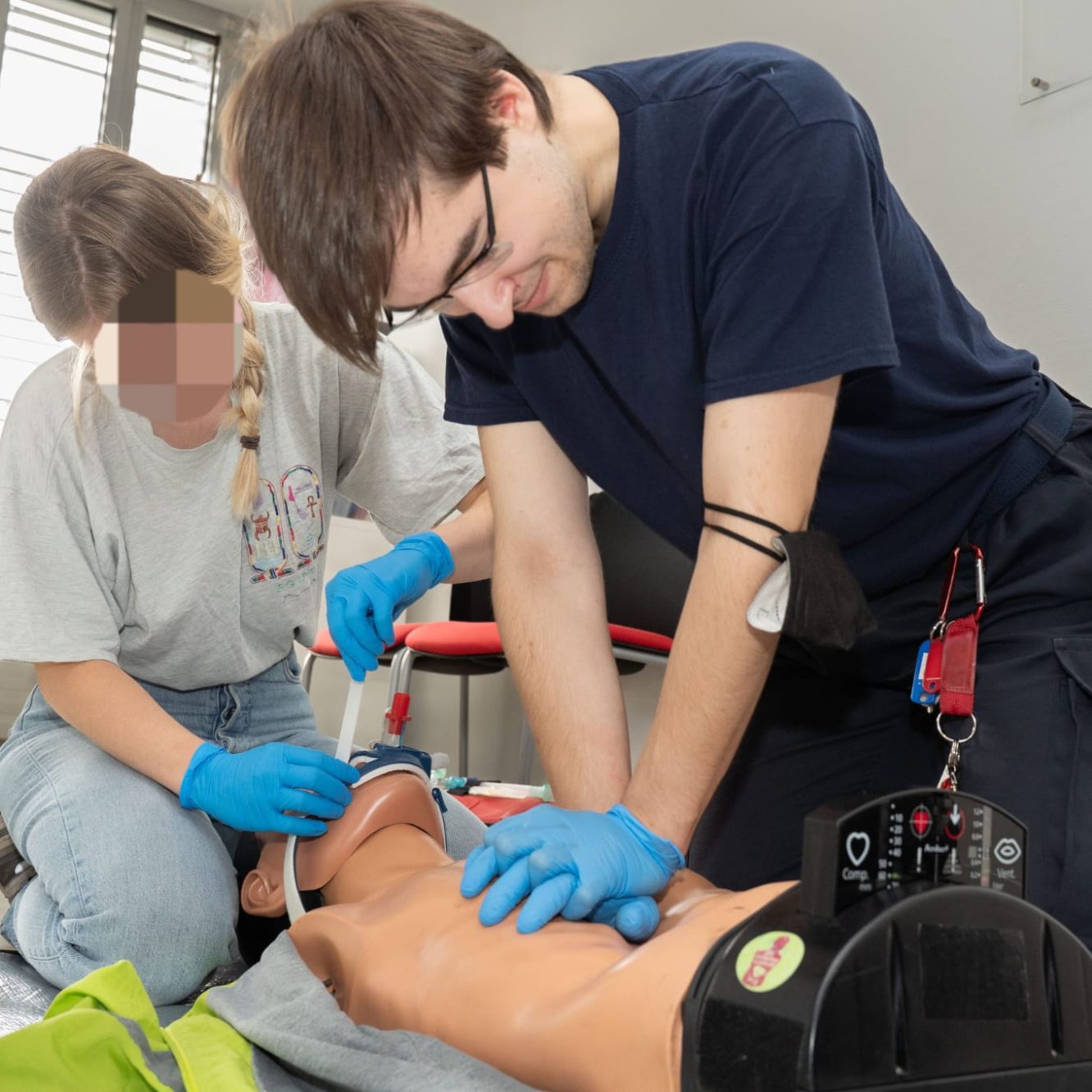 Medizinisches Training: Rettungssanitäter führt Herzdruckmassage an einer liegenden Puppe durch. Eine andere Sanitäter*in intubiert.