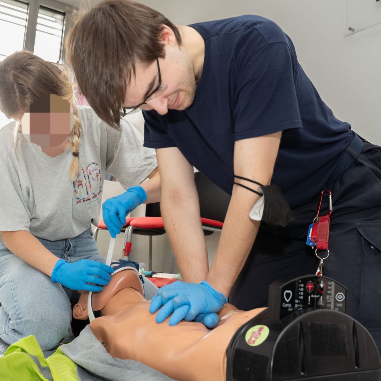 Medizinisches Training: Rettungssanitäter führt Herzdruckmassage an einer liegenden Person durch. Eine andere Sanitäterin intubiert.