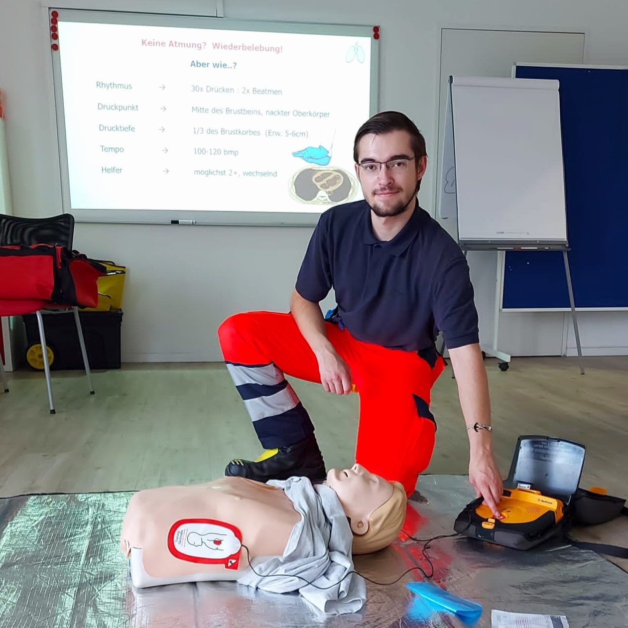 Ein Sanitäter demonstriert Erste-Hilfe-Maßnahmen inkl. AED an einer Übungspuppe in einem Raum der für Notfalltrainings genutzt wird.