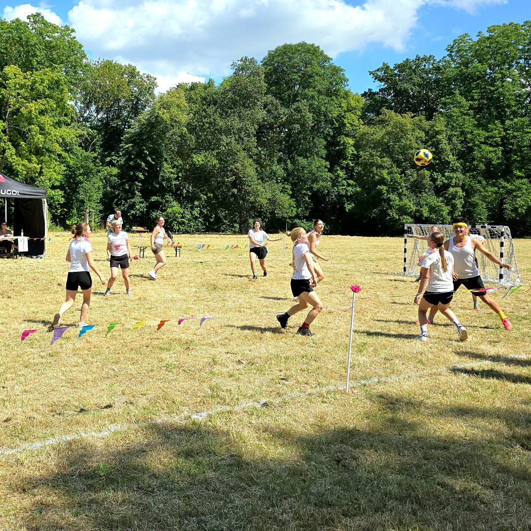 Eine Gruppe von Personen spiel Discofoot (getanzter Fußball) auf einem abgesteckten Spielfeld. Eine Jury bewertet das Spiel.