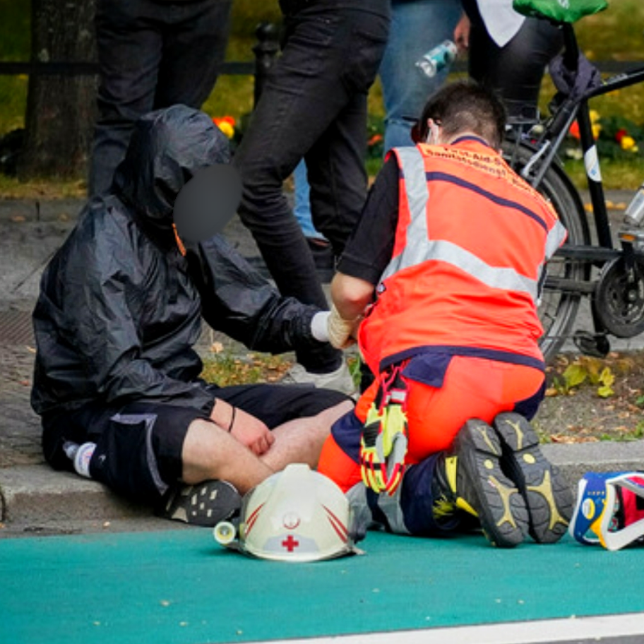 Ein Sanitäter in Einsatzkleidung versorgt eine verletzte Person neben einer Sitzblockade bei einer Demonstration.