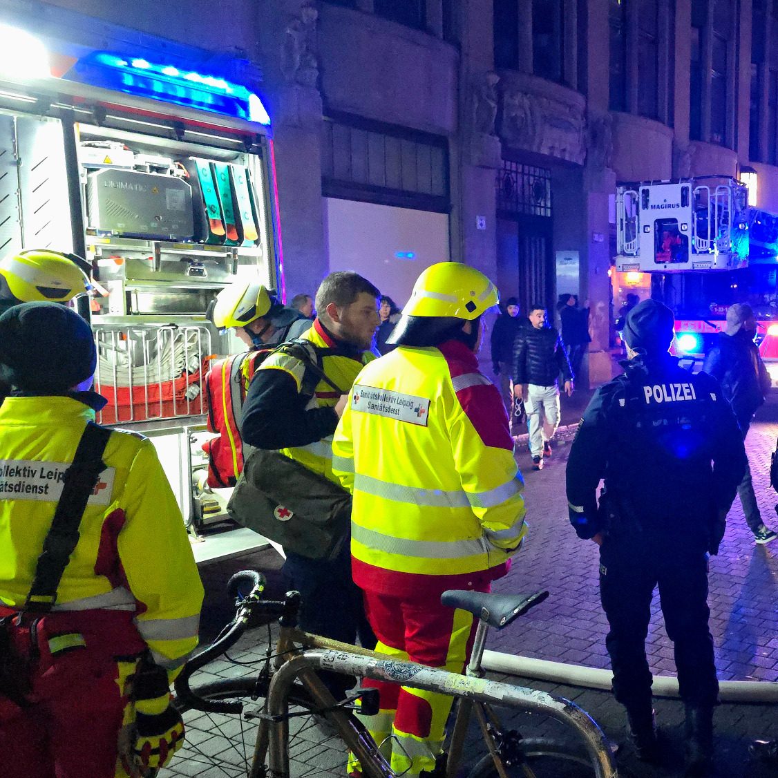 Einsatzkräfte des SKL sind zusammen mit Feuerwehr/Polizei im Einsatz und helfen bei einem Hotelbrand. Im Hintergrund stehen Löschfahrzeuge.
