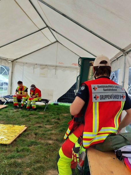 Ein Gruppenführer protokolliert einen Einsatz. Zwei Sanitäter*innen sitzen in der Unfallhilfsstelle.