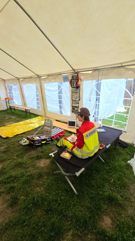 Ein Sanitäter sitze auf einer Liege in der Unfallhilfsstelle. Um ihn herum befindet sich medizinisches Material. Er schreibt etwas.