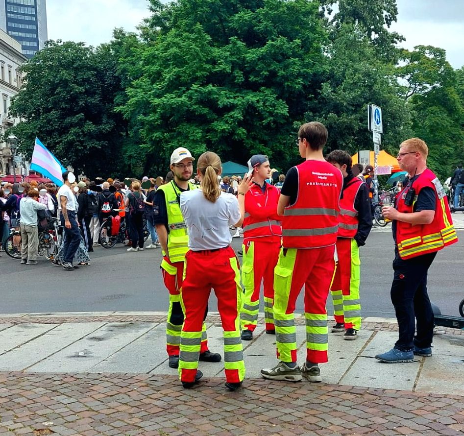 Gruppe von Sanitäter*innen steht in Einsatzkleidung am Rand einer Demo und bespricht sich für den Einsatz.