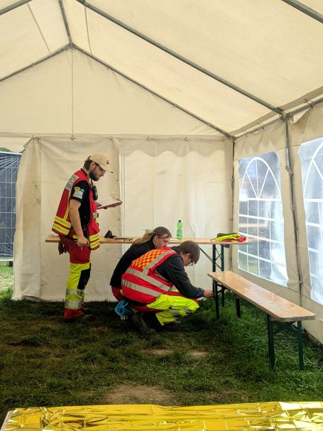 Zwei Sanitäter*innen führen eine Sichtung bei einem MANV durch (Übung). Ein Ausbilder steht hinter ihnen und prüft deren Handlung.