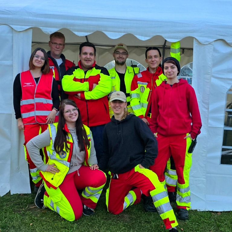 Ein Team aus mehreren Helfer*innen des Sanitätskollektiv Leipzig steht in Einsatzkleidung vor einer Unfallhilfsstelle auf einem Konzert.