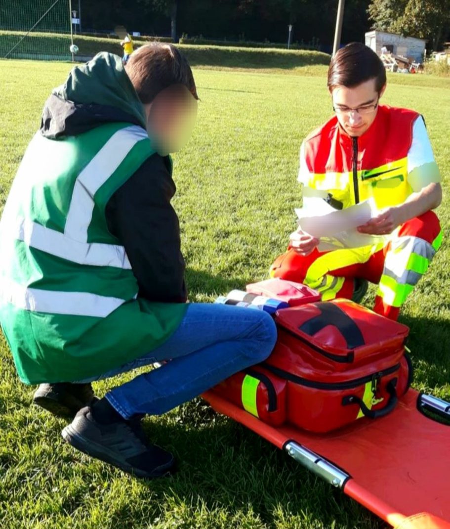 Ein Sanitäter im Liegendtransport und ein Helfer besprechen die Behandlung eines Patienten.