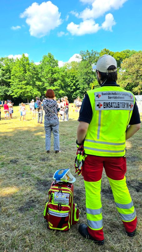 Ein Sanitäter beobachtet das laufende Spiel beim Discofoo Open Air Leipzig. Er trägt eine gelbe Weste auf der "Einsatzleiter*in" steht.